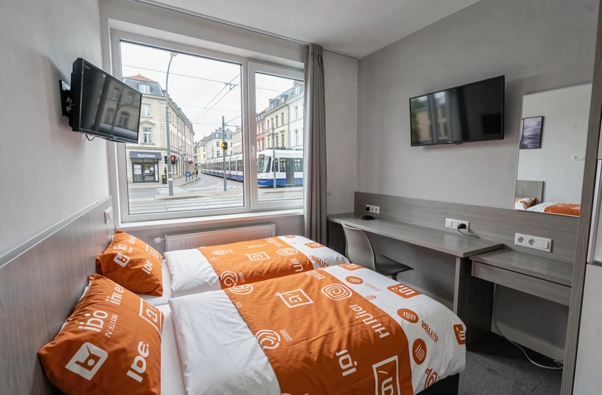 Chambre fonctionnelle et compacte d'un hôtel Ibis Budget au centre de Lille avec literie blanche et orange